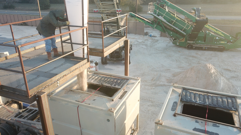 Worker loading wet frac sand into on-site containers at a mining facility.