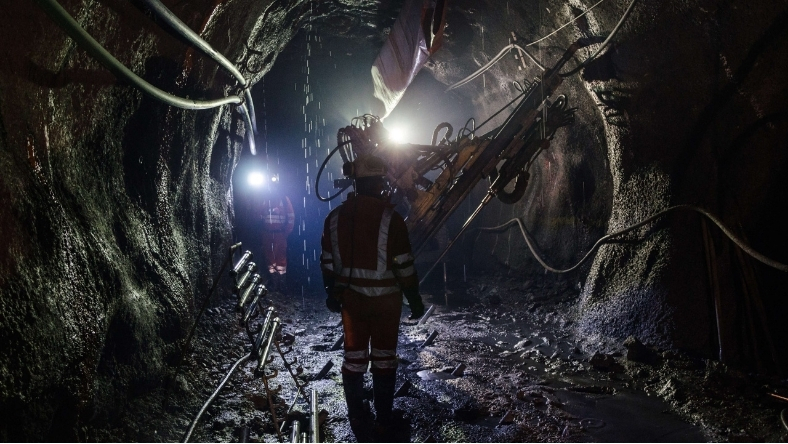 Underground mine worker operating drilling equipment in a low-light tunnel